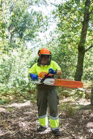 A worker with a chainsaw stands in full protective gear.